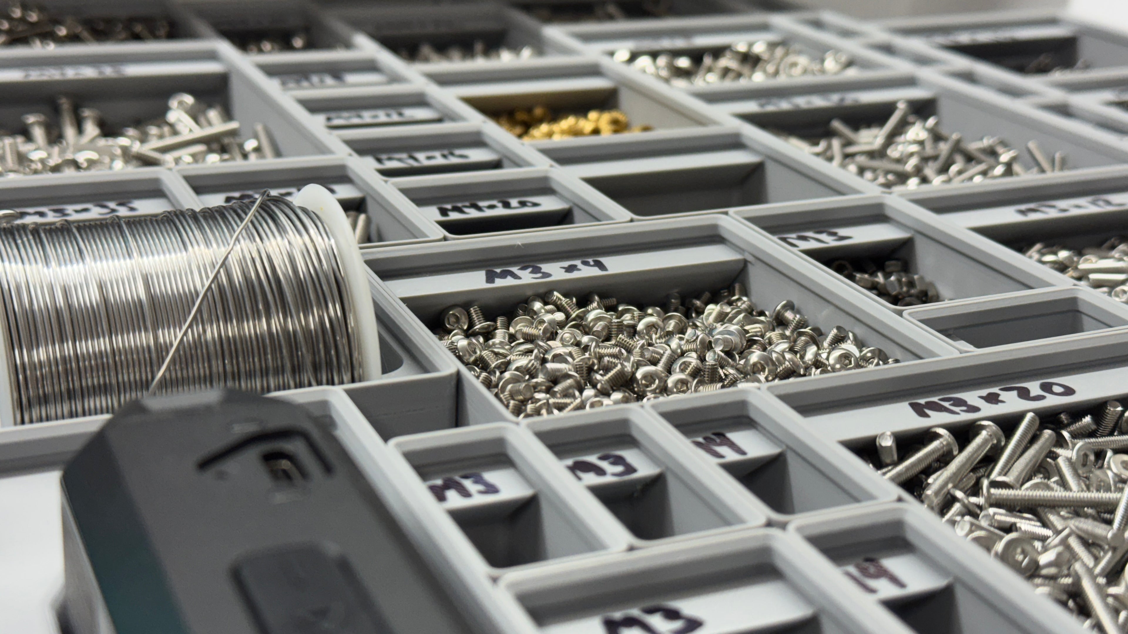 Gray storage organizer with compartments filled with various small hardware items.